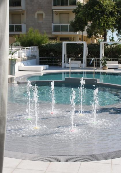 Piscina con fontane e lettini bianchi, circondata da piante.