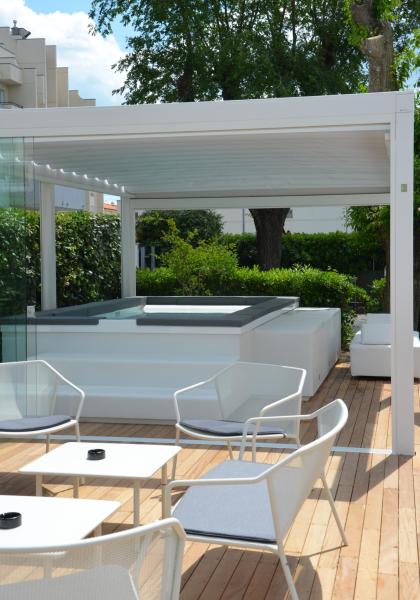 Elegant terrace with hot tub, modern chairs, and lush greenery.
