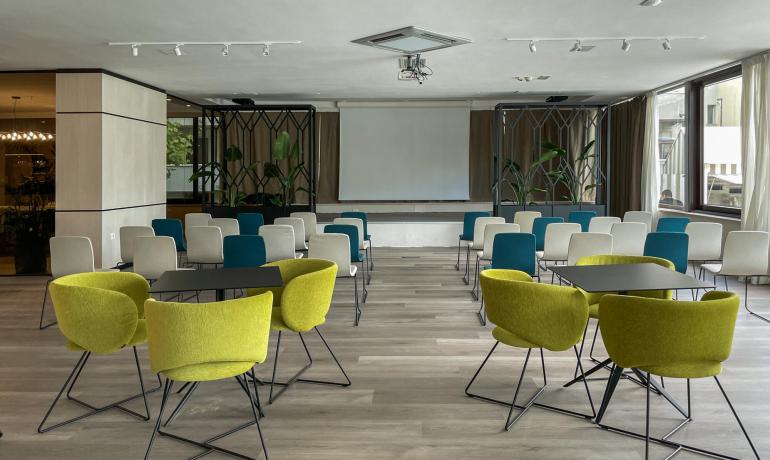 Sala conferenze moderna con sedie colorate e proiettore.