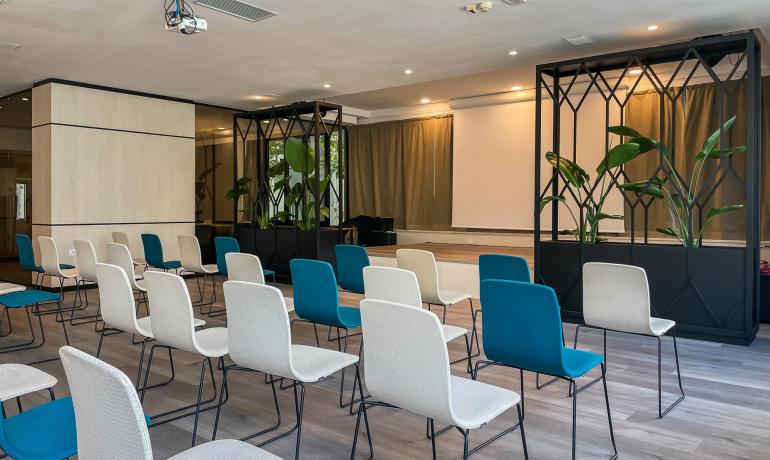 Sala conferenze moderna con sedie colorate e piante decorative.