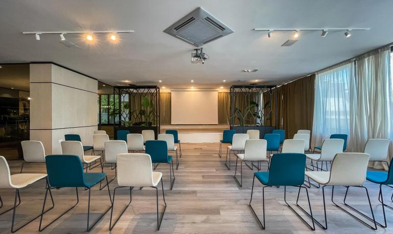 Sala conferenze moderna con sedie colorate e schermo.