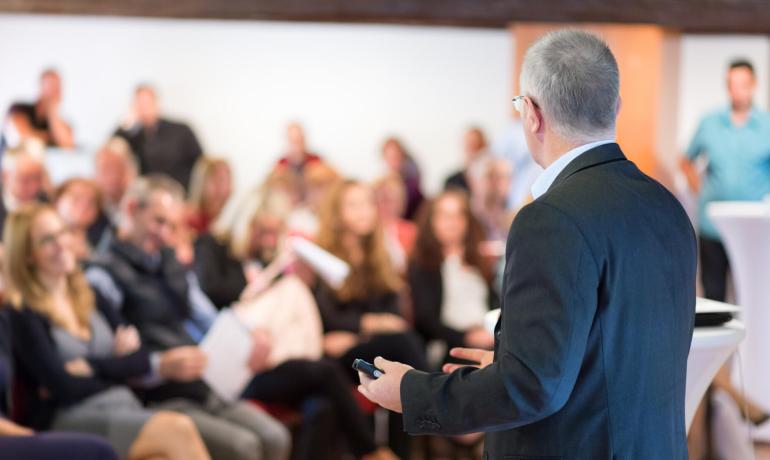 Uomo che parla a una platea di persone durante una conferenza.