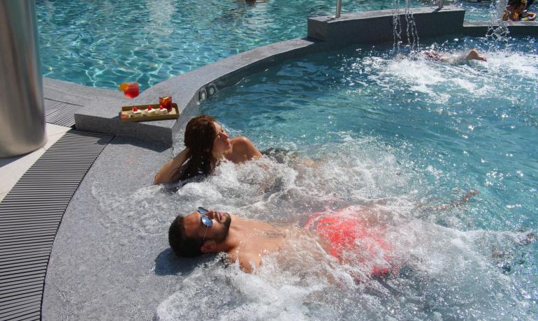 Persone rilassate in piscina con drink e dolci.