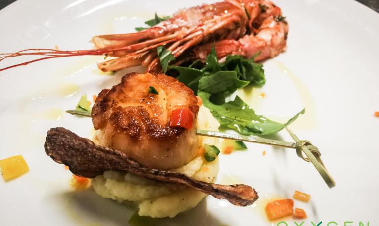 Piatto gourmet con capesante, gamberi e verdure su purè di patate.