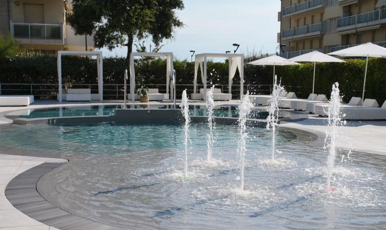 Piscina elegante con fontane e lettini bianchi.