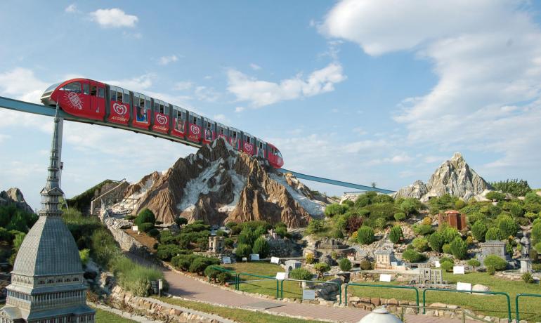 Monorotaia rossa sopra un paesaggio in miniatura con montagne e edifici.