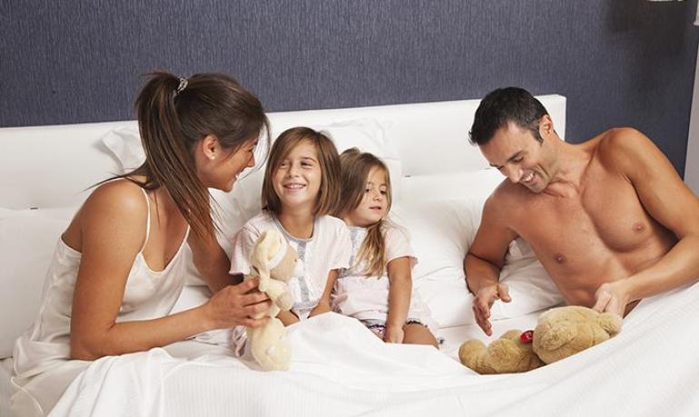 Famiglia felice a letto, sorrisi e tenerezza con peluche.