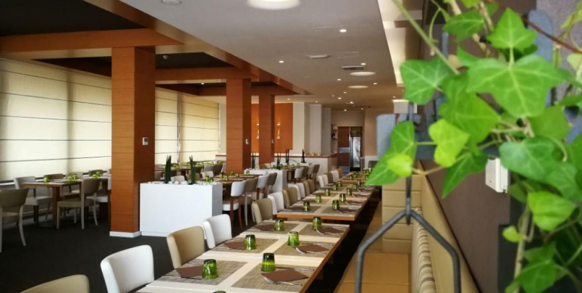 Modern restaurant with set tables and decorative plants.