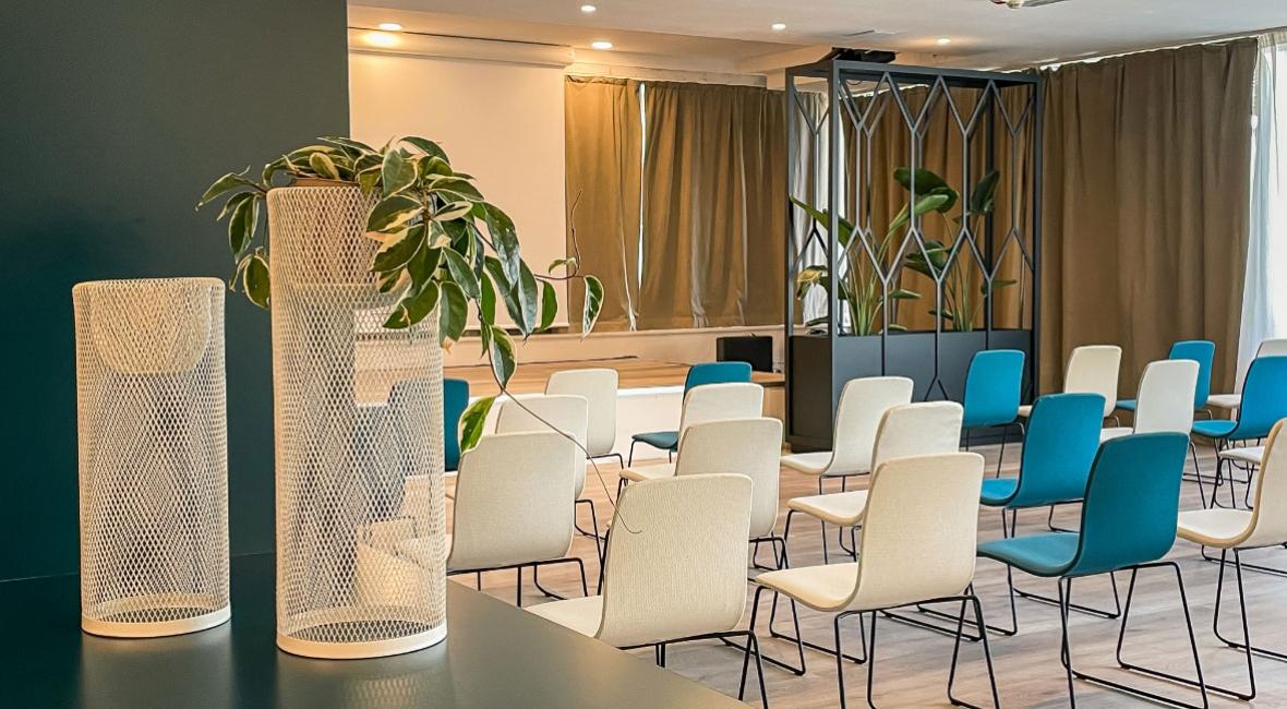 Sala conferenze moderna con sedie colorate e decorazioni verdi.