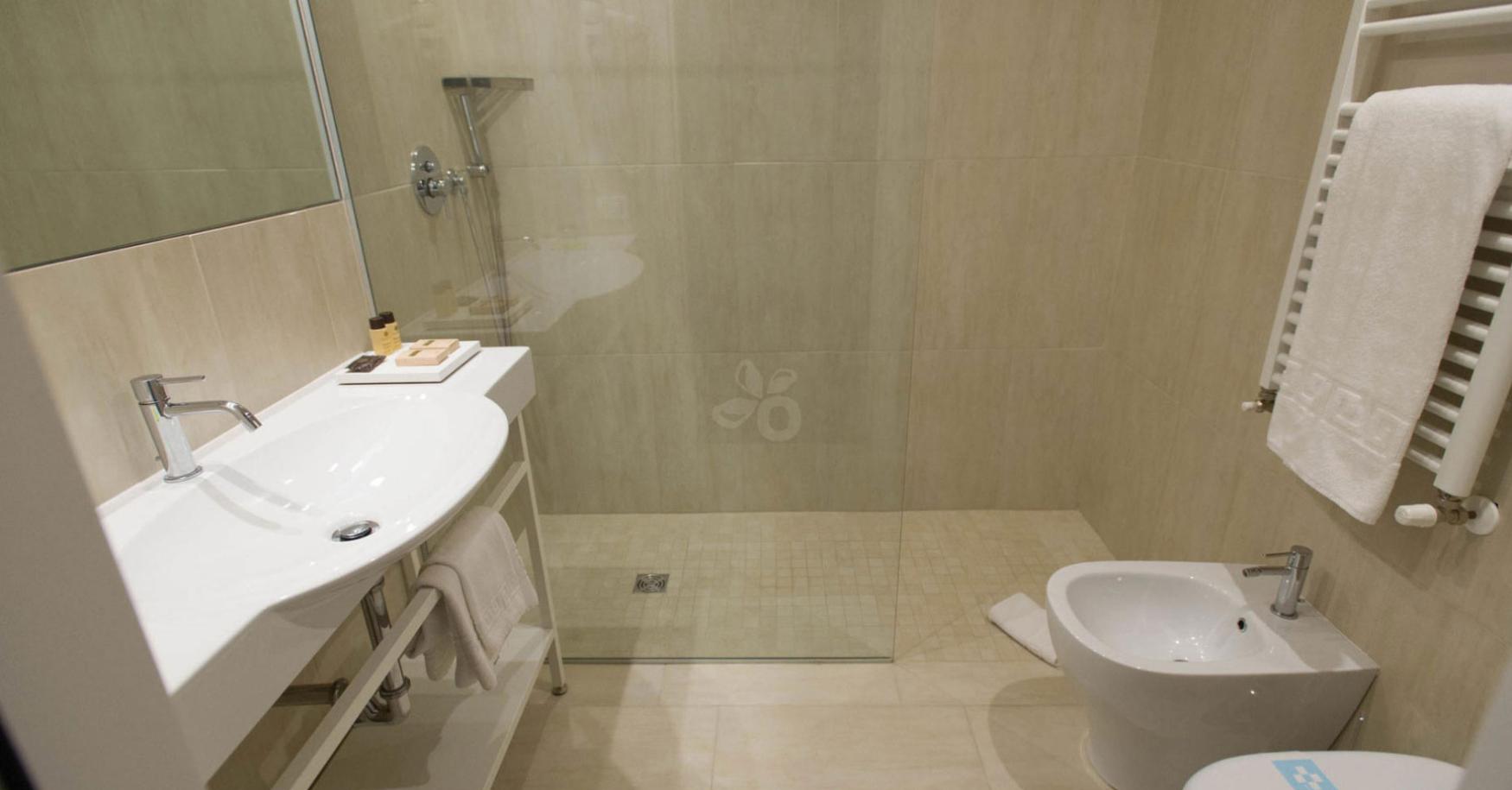 Modern bathroom with shower, sink, bidet, and white towels.