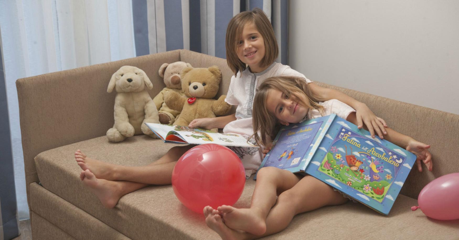 Deux filles lisent des livres sur un canapé avec des peluches et des ballons.