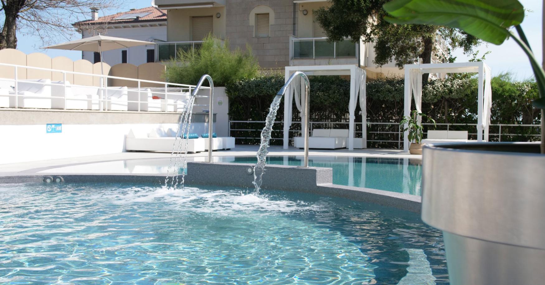Piscina con sedie a sdraio e fontane in un ambiente moderno.