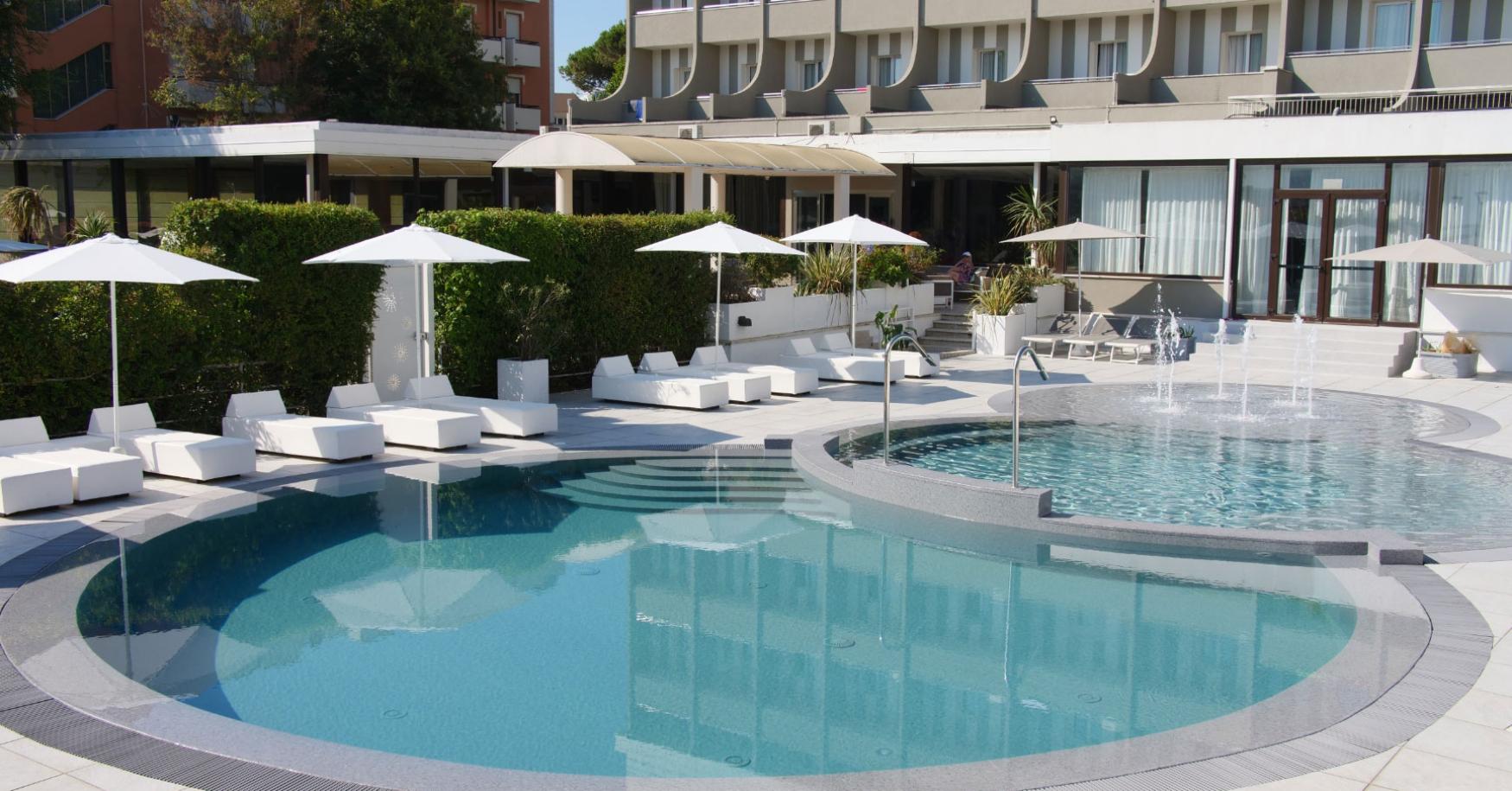Piscina all'aperto con lettini e ombrelloni bianchi in un hotel moderno.