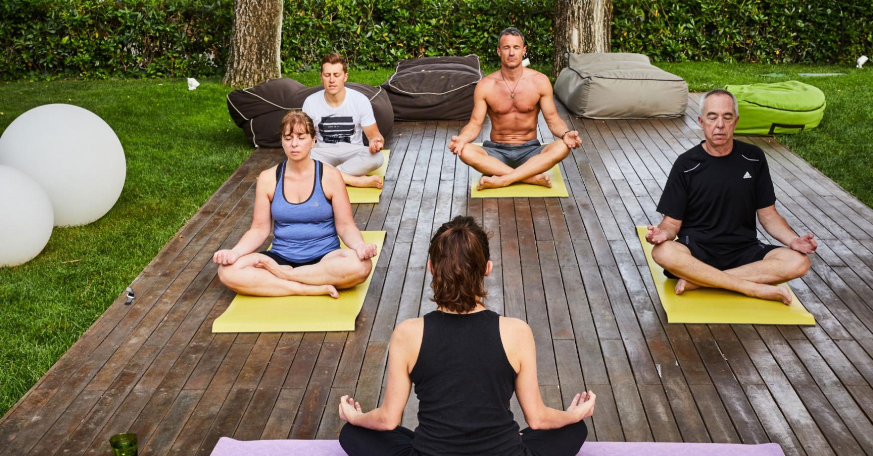 Outdoor yoga class with five people on mats.