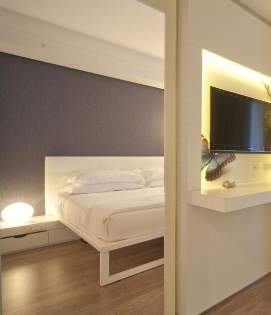 Camera moderna con letto bianco e TV a parete.