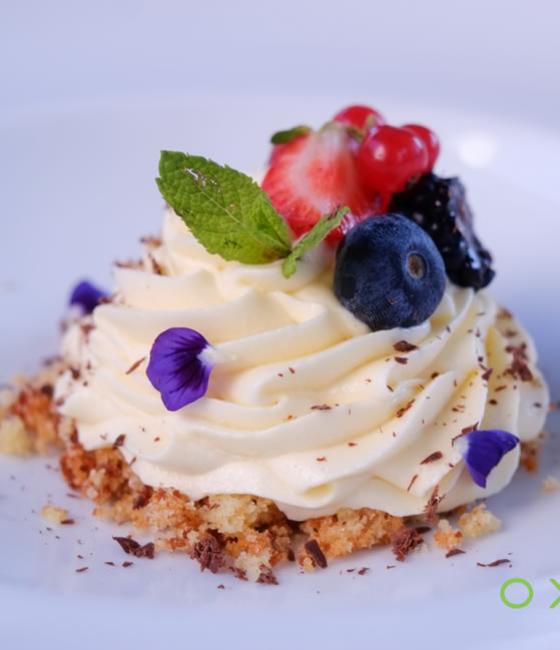 Dolce alla crema con frutti di bosco e decorazioni floreali.