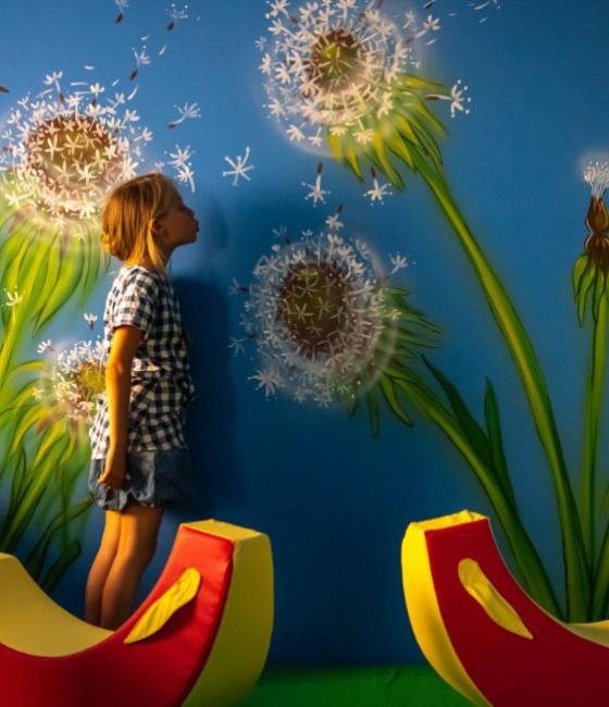 Bambina che soffia su un murale di soffioni in un'area giochi.