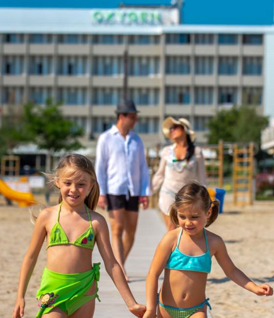 Zwei Mädchen gehen am Strand, gefolgt von ihren Eltern.