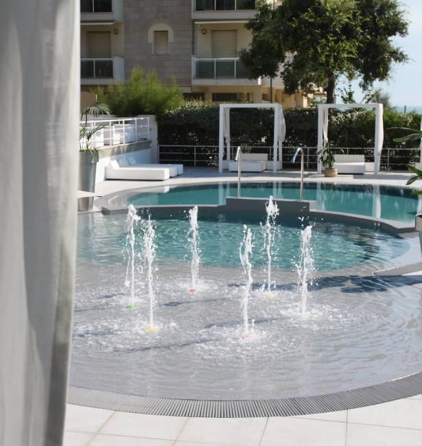 Piscina con fontane e lettini, circondata da vegetazione.